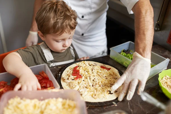 Boy puts tomatoes on  pizza — Stock Photo, Image