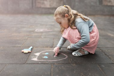 little girl draws chalk on asphalt