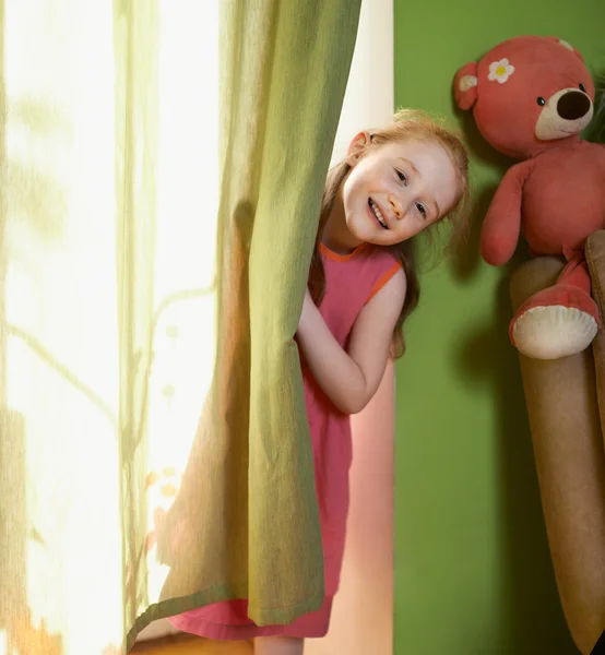 Little girl peeking out from behind curtains — Stock Photo, Image