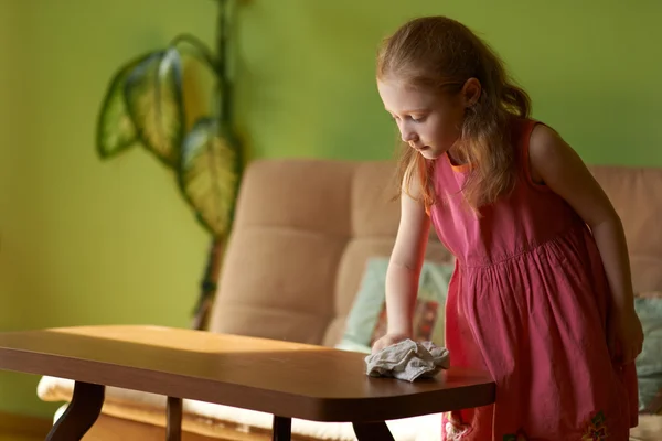 Маленькая девочка чистит пыль на столе — стоковое фото