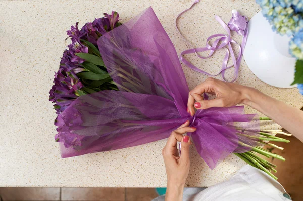 Woman tying a bow on  bouquet of purple flowers — Stock Photo, Image