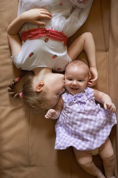 Older sister kissing the younger lying on  couch — Stok fotoğraf