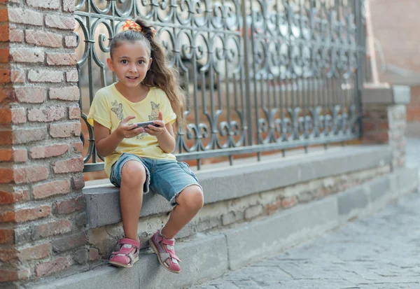 Девушка сидит на улице и играет в телефон — стоковое фото