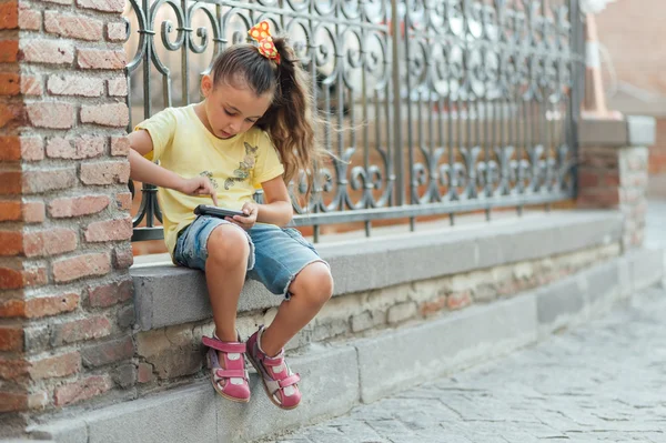 Malá dívka sedí venkovní a přehrávání na telefonu — Stock fotografie