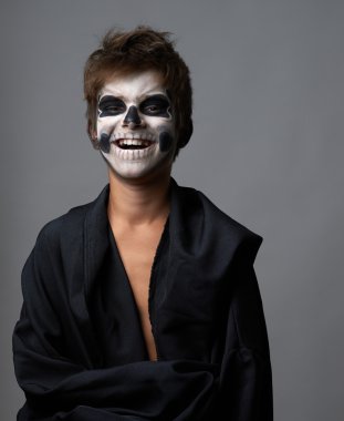 Teen with make-up of the skull in a black cloak laughs clipart