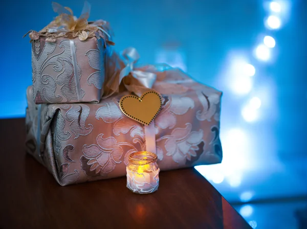 Beautiful gifts stand on  table beside a candle — Stock Photo, Image