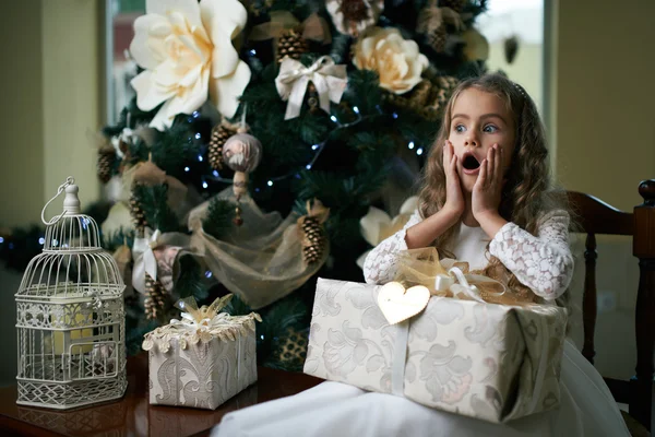 Menina senta-se perto de uma árvore de Natal com presente . — Fotografia de Stock