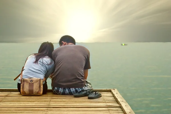 Pareja en el tiempo de puesta del sol sentado en el puente de madera en el camino a — Foto de Stock