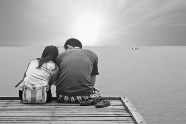 Casal no pôr do sol tempo sentado na ponte de madeira no caminho para — Fotografia de Stock