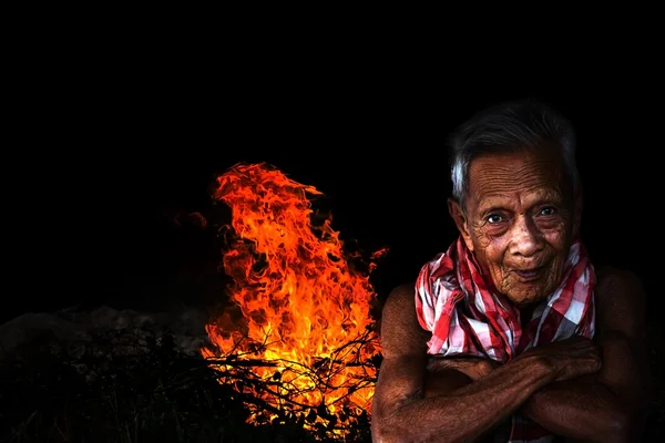 Smiling old man sitting by the fire — Stock Photo, Image
