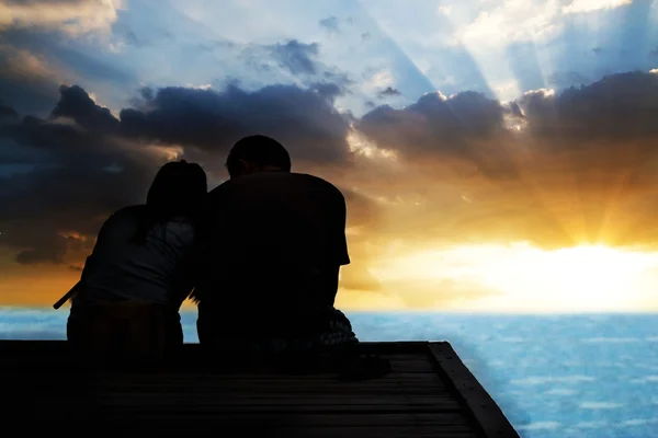 Casal no pôr do sol tempo sentado na ponte de madeira no caminho para — Fotografia de Stock