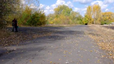 Taşra yolunda yürüyen ve elinde eski yeşil bir bavul tutan yaşlı bir adam.