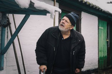 Ahırının yanında duran ve kar yağdıktan sonra çatıyı inceleyen Ukraynalı yaşlı köylünün klasik portresi.