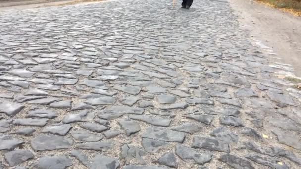 Idősebb ember lassan sétál a macskaköves úton fonott kézzel készített sétapálcával