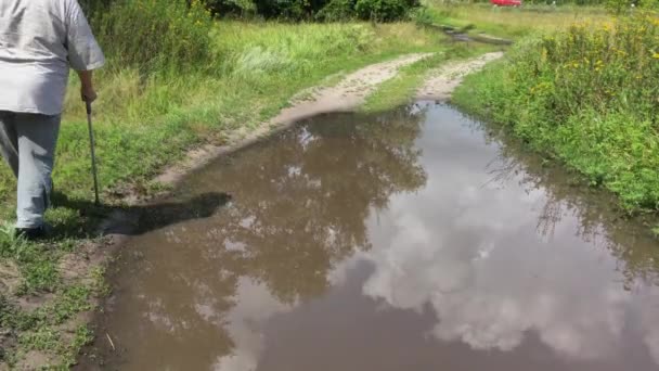 乌克兰沙地乡间道路上 一个拿着手杖缓缓走过大水坑的残疾老人 — 图库视频影像