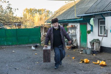 Pozitif Ukraynalı yaşlı köylü çiftlikte yürürken büyük antik bir sandık taşıyor.