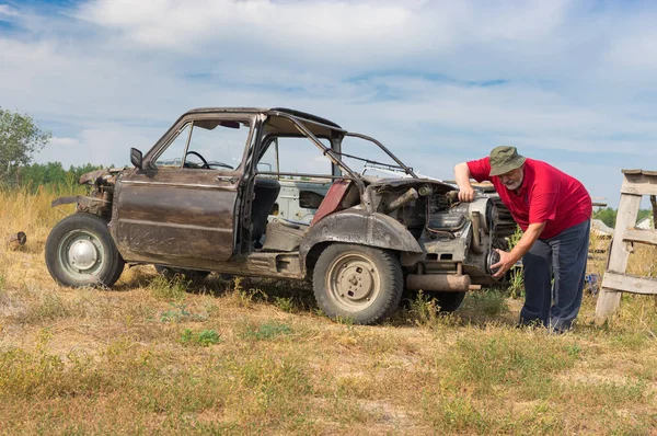 Senior Mann Begutachtet Selbstgebautes Auto Aus Verschiedenen Alten Fahrzeugen lizenzfreie Stockfotos