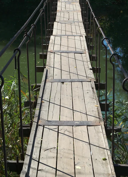 Vecchio ponte pedonale in legno appeso su un piccolo fiume — Foto Stock