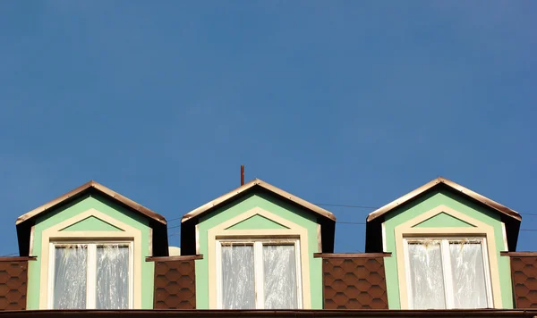 Trzy okna na poddaszu na dachu na tle błękitnego nieba. — Zdjęcie stockowe