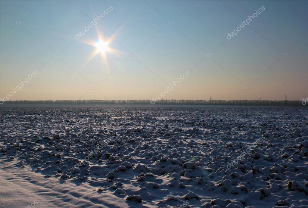 Sonne über einem gepflügten Feld, das mit Schnee bedeckt ...