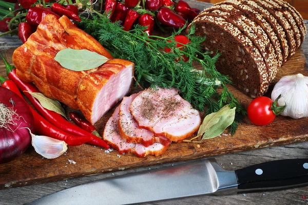 Ветчина и хлеб, нарезанные ножом. Зеленые и красные овощи на доске — стоковое фото