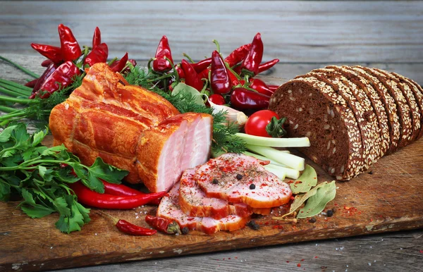 Нарезанные ветчина и хлеб с зелеными и красными овощами на доске — стоковое фото