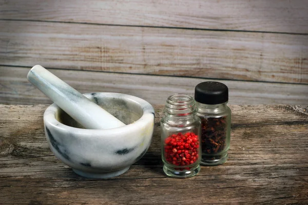 Marble mortar and pestle on old wooden table. Small glass jars with pepper and cloves