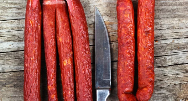 Smoked sausages and knife on wooden background — Stock Photo, Image