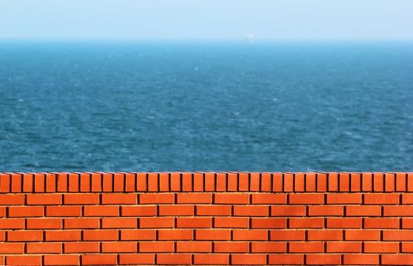 Червона цегляна стіна на фоні синього моря . — стокове фото