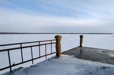 Donmuş bir nehrin üzerinde kırık parmaklıkları olan terk edilmiş eski bir köprünün detayları.