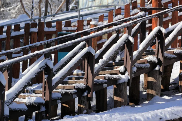 Snow on wooden fences, benches and handrails in a park on a sunny winter day