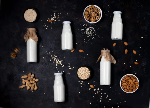 bottles of vegan plant-based milk made from seeds and nuts. flat lay on black background.