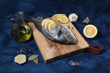 Mavi arka planda ahşap bir tahtada taze dorado balığı. Zeytinyağı, limon, kırmızı biber, sarımsak, tuz, biber pişiriyorum. Akdeniz diyetinin yemeği.