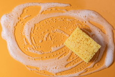 Sabunla temizlik süngeri. Sarı arka planda köpük köpüklü doku. kopyalama alanı. Süngerle temizlik..