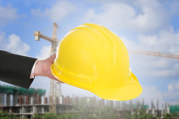 hand of engineer holding helmet with construction crane backgrou