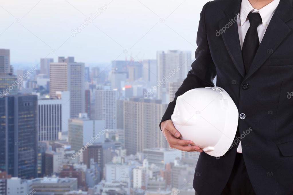 engineer holding white helmet with city background