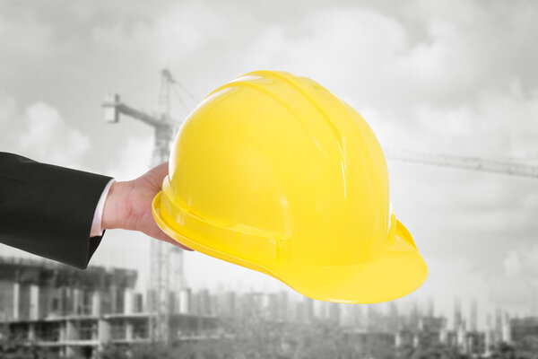 hand of engineer holding helmet with construction crane backgrou