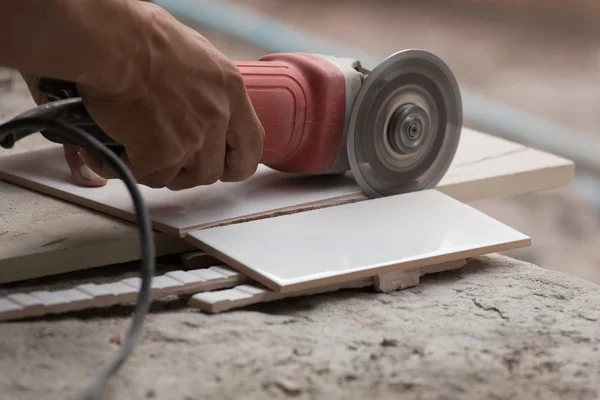 Bauarbeiter schneidet eine Fliese mit einem Winkelschleifer — Stockfoto