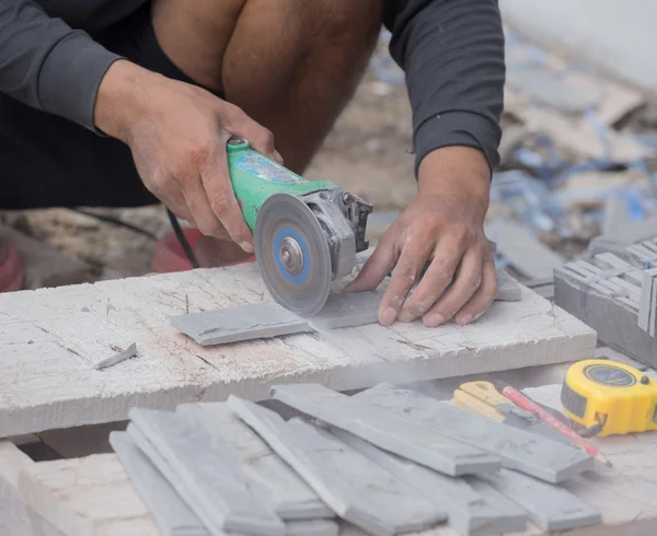 Trabajador cortar una baldosa de piedra arenisca utilizando una amoladora angular — Foto de Stock