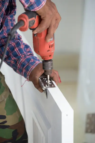 Instalação da porta. Trabalhador faz um buraco para parafuso de dobradiça — Fotografia de Stock
