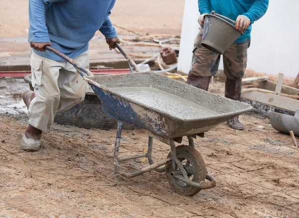 Trabajador empujando carretilla con cemento húmedo para verter piso de hormigón — Foto de Stock