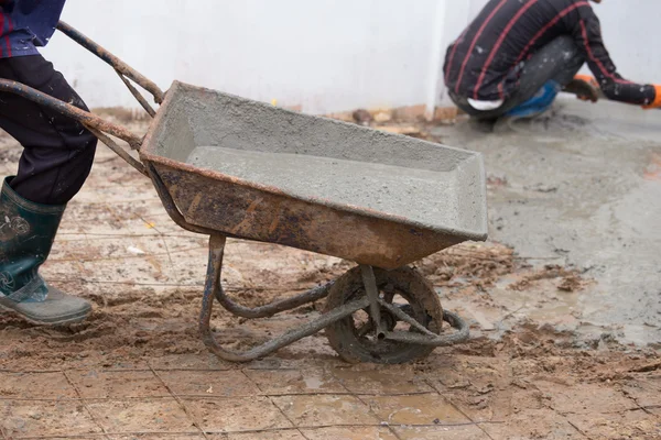Werknemer duwen barrow met nat cement te gieten van de betonnen vloer — Stockfoto