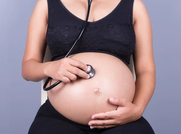 Close-up da mulher grávida com estetoscópio ouvindo barriga a b — Fotografia de Stock
