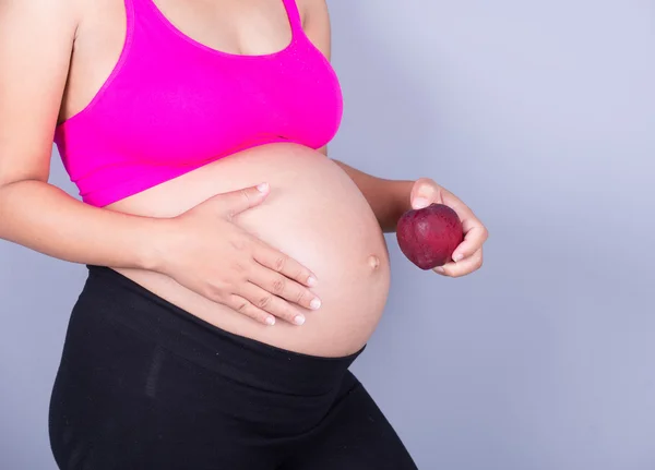 Barriga de close-up da mulher grávida com maçã vermelha em backgrou cinza — Fotografia de Stock
