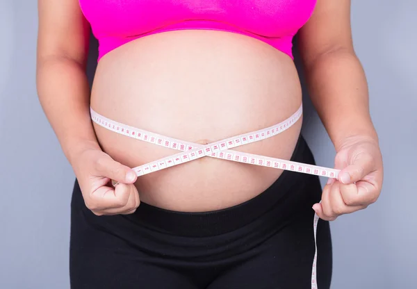 Barriga close-up de mulher grávida com fita métrica no bac cinza — Fotografia de Stock