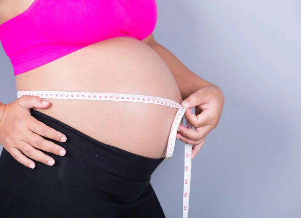 Barriga close-up de mulher grávida com fita métrica no bac cinza — Fotografia de Stock