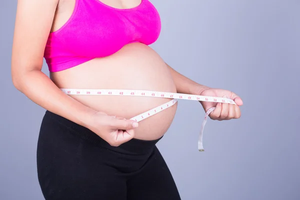 Barriga close-up de mulher grávida com fita métrica no bac cinza — Fotografia de Stock