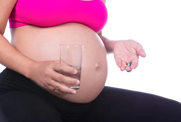 Primo piano della mano della donna incinta con bicchiere d'acqua e pillola — Foto Stock