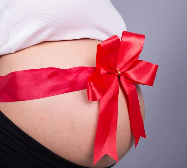 Fechar a mulher grávida com fita vermelha presente na barriga — Fotografia de Stock
