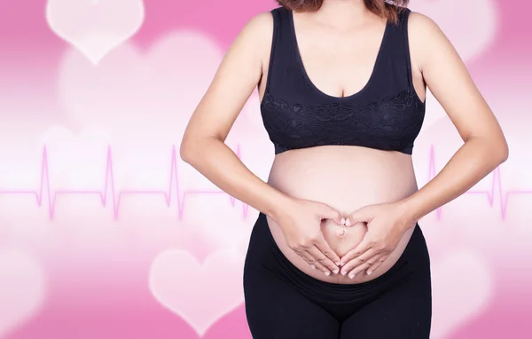 Έγκυος γυναίκα κρατώντας τα χέρια της σε σχήμα καρδιάς στην κοιλιά σε αυτός — Φωτογραφία Αρχείου